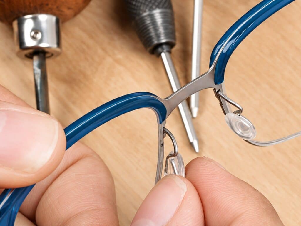 ajustement d’une plaquette de nez sur une monture de lunettes bleue dans un atelier d’opticien